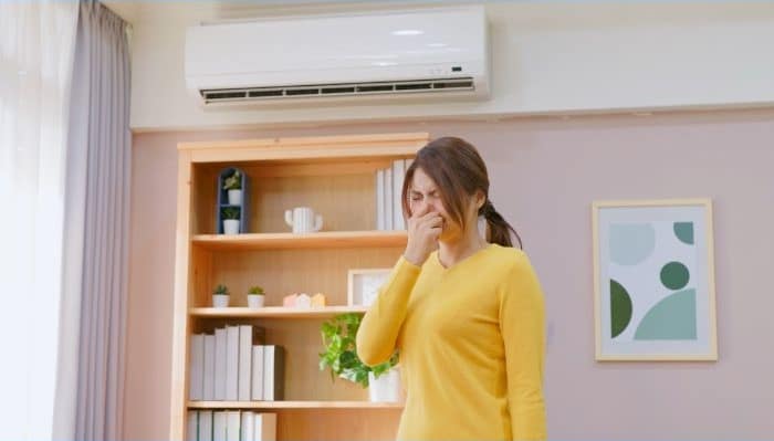 woman holding nose in front of mini-split AC emitting a smell